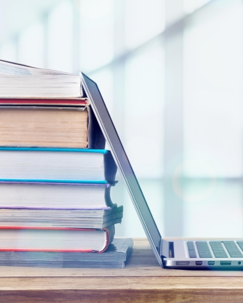 Stack of books with laptop on wooden table